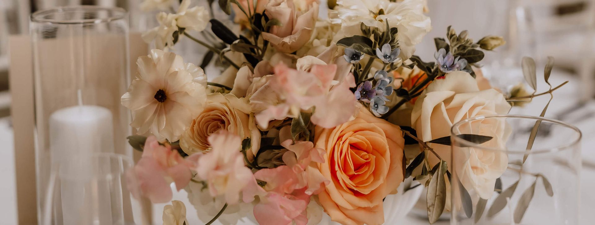 Eine Vase mit Blumen steht auf einem Tisch, umgeben von Gläsern und Kerzen.