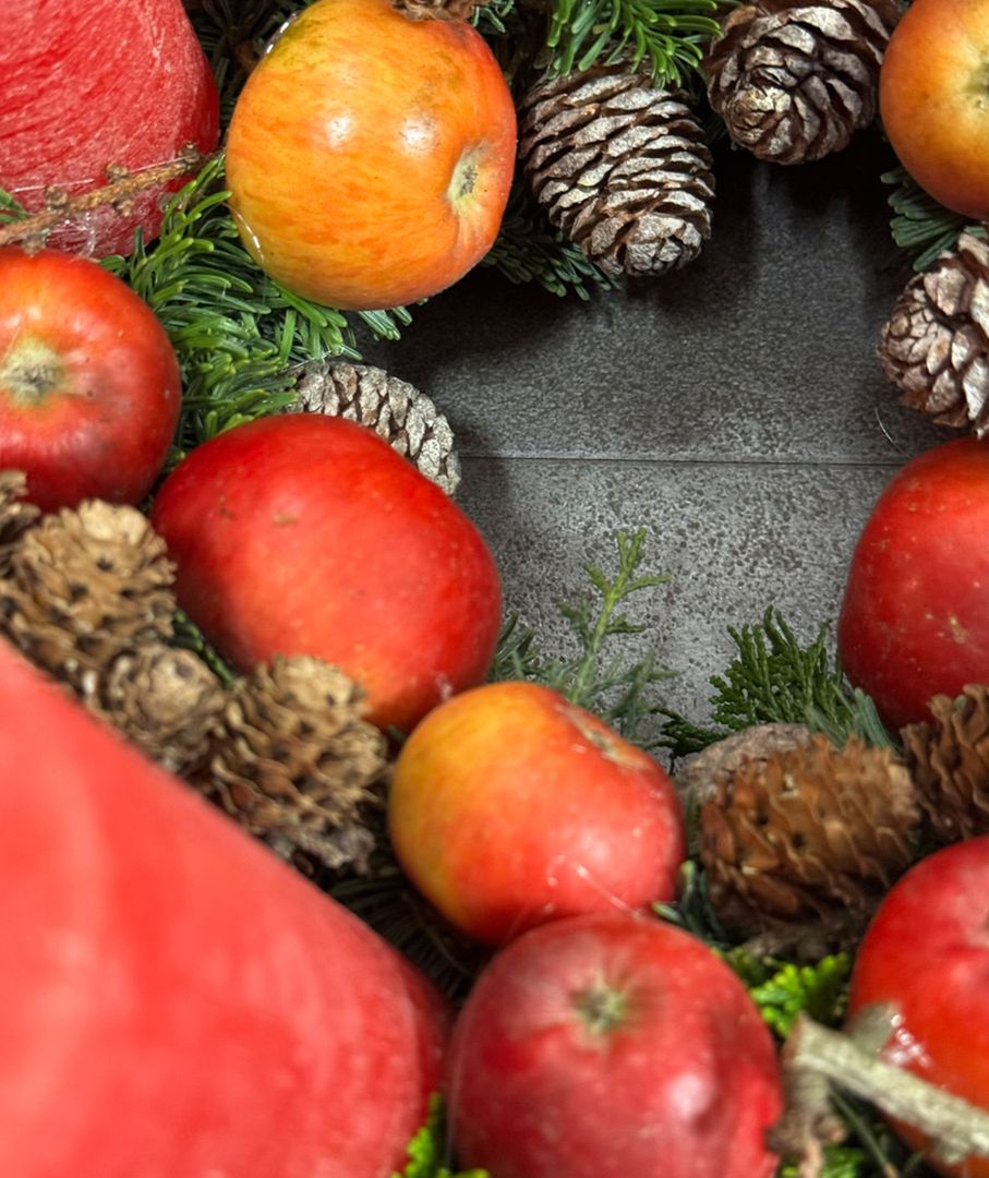 Ein dekorativer Kranz, geschmückt mit Äpfeln, Tannenzapfen und immergrünen Zweigen, passend für die kalte Jahreszeit.