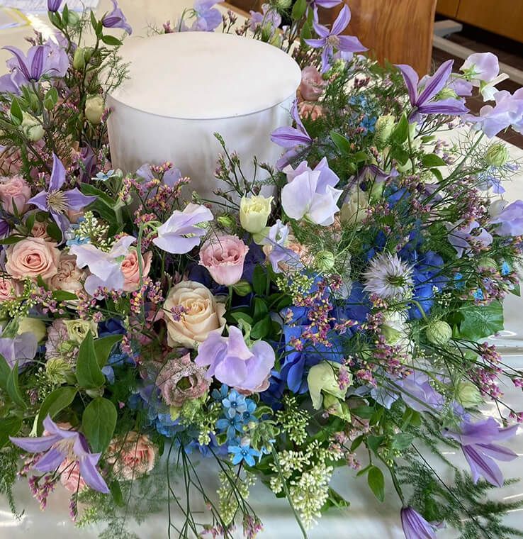 Eine Urne, die von sehr vielen verschiedenen Blumen umgeben ist.