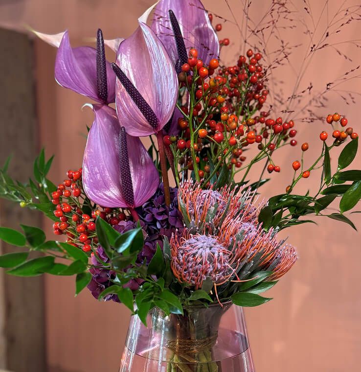 Eine Vase mit lila Blumen und roten Beeren